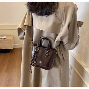Detail of dark brown glossy patent leather bucket bag with metallic logo and tassel