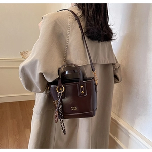 Detail of a shiny chocolate brown bucket bag with gold hardware and a striped charm