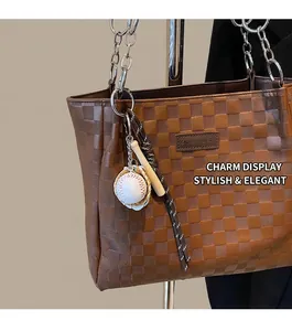 Detail of a baseball charm with a mini bat on a brown checkered tote bag's silver chain