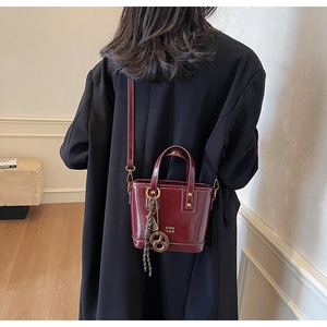 Detail of burgundy patent leather bucket bag with metallic gold zipper and charm