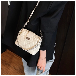 Détail d'un sac matelassé crème avec chaîne porté sur une veste de tailleur noire