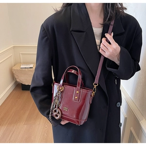 Detail of burgundy glossy leather bucket bag with metallic logo and fashion charm