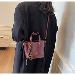 Detailed view of deep red bucket bag in polished leather with gold hardware on model