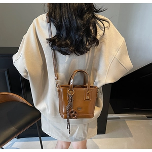 Detail of glossy brown patent leather bag with embossed logo and metal charm pendant