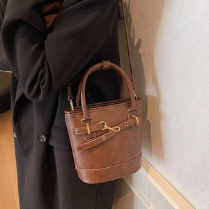 Sac seau marron vintage avec texture litchi et boucle dorée porté sur manteau