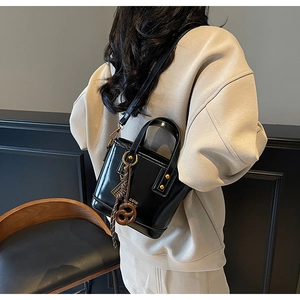 Detail of a black glossy leather bucket bag featuring gold hardware and a pretzel charm