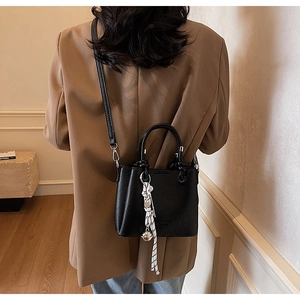 Detail of black litchi grain leather tote bag with woven pendant and silver charm
