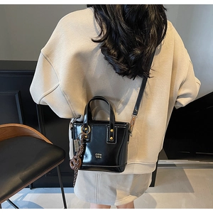 Detailed view of a black leather bucket bag with gold logo and woven charm on a model