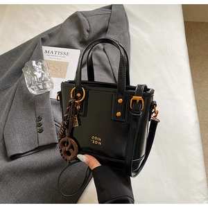 Detail of black patent leather bucket bag with gold logo and decorative charms on a blazer