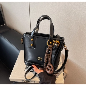 Detail of black glossy handbag with gold rivets and pretzel charm on a book