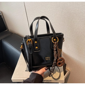 Detail of black glossy crossbody bucket bag with gold lettering and pretzel charm