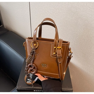 Close-up of brown faux leather tote bag with gold metal logo and knotted tassel charm