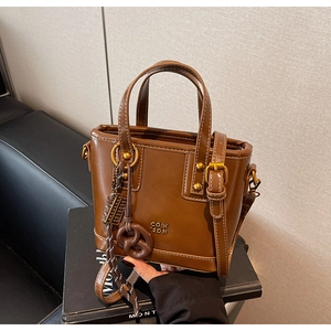 Detail of caramel brown matte leather tote with gold logo and twisted knot charm