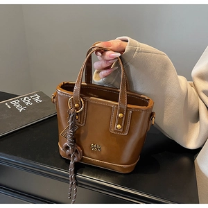 Detail of a mini brown PU bucket bag featuring golden ring hardware and chic knot charm