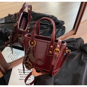 Detail of dark burgundy patent leather bucket bag with gold hardware and tassel charm