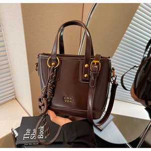 Detail of dark brown tote bag with woven tassel and gold COIH 2DN logo on glossy leather