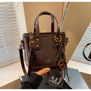 Detail of dark brown patent leather bucket bag with gold branding and bow accessory