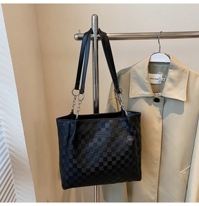 Detail of black woven checkerboard tote bag with metal chain handle and leather tag