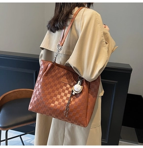 Detail of a brown checkered tote bag featuring a logo patch and a white pompom charm