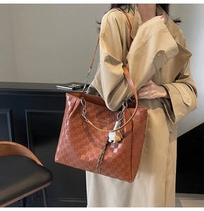 Brown checkered tote bag with metal chain detail and doll charm on a khaki trench coat