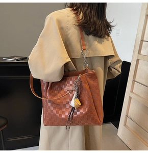 Detail of brown checkered tote bag with leaf charm and leather shoulder strap on model