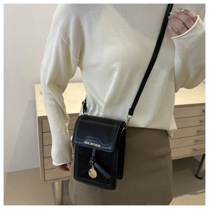 Dettaglio mini borsa a tracolla nera con testo dorato e ciondolo indossata da una modella