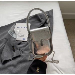 Detail of silver textured mini bag with metallic finish and chain on a stylish bed setting