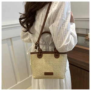 Detail of hand-woven straw tote with brown leather handles and adjustable shoulder strap
