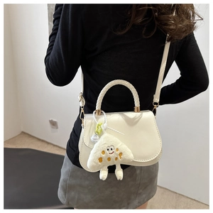 Detail of white PU leather crossbody bag featuring a plush mushroom charm and woven handle