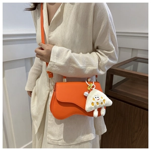 Detail of orange wavy-flap crossbody bag with white plush charm on thin leather strap