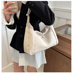 Detail of beige hobo shoulder bag with metal snap pocket worn by a model in a suit