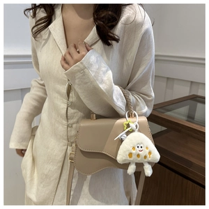 Detail of a beige crossbody bag featuring wavy base design and plush mushroom charm