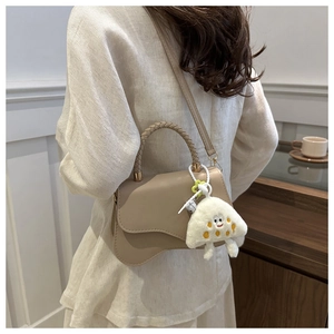 Detail of beige leather crossbody bag with woven handle and plush charm on a model