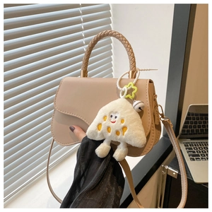 Detail of beige saddle bag featuring a woven top handle and cute plush triangle pendant