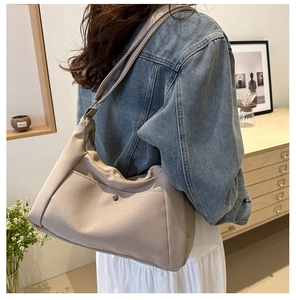 Detail view of beige canvas tote bag with metal magnetic buckle on a model shoulder