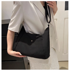 Détail du sac cabas en tissu noir avec boucle argentée sur une tenue de blazer blanc