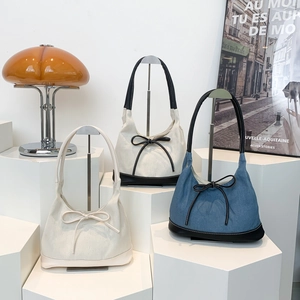 Three bow-tie hobo tote bags in white and denim fabric displayed on minimalist pedestals