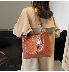 Macro detail of the woven leather texture and metal chain strap on this brown tote bag