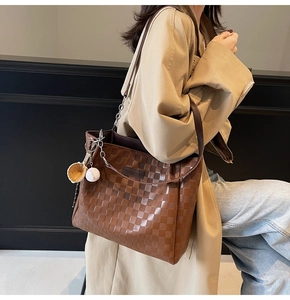 Close-up of brown checkered tote bag with a baseball glove charm and leather strap