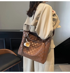 Brown checkered tote bag with silver chain worn by a model in a beige trench coat