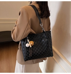 Detail of black checkered tote bag featuring a leather chain strap and baseball charm