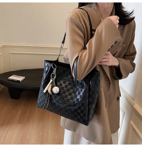 Detail of checkered tote bag with baseball charm and metallic chain strap worn by a model