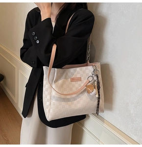 Close-up of cream checkerboard tote bag with baseball charm and leather logo tag