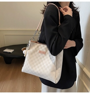 Detail of white checkered tote bag with pink leather label and elegant metal chain strap