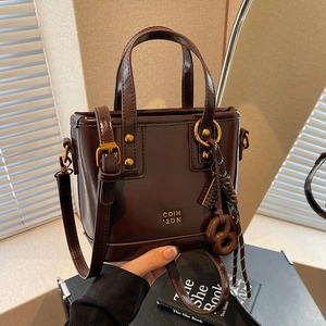 Deep brown patent leather tote bag with gold rivets and pretzel charm held by hand
