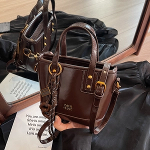 Dark brown retro bucket bag with gold hardware and top handles shown on a mirrored surface