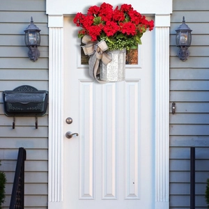 Christmas hanging basket with red geraniums, green leaves and a rustic bow on a white door