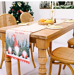 Detail eines Weihnachts-Tischläufers mit Gnom-Druck, roten Bommeln und Merry Christmas Text