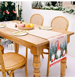 Detail eines Weihnachts-Tischläufers mit Gnomen-Print, Schriftzug und roten Bommel-Verzierungen