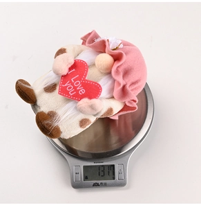 Close-up of a pink Valentine's gnome doll holding a red heart on a digital scale